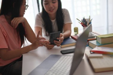 Evde ders çalışırken akıllı telefon kullanan iki kız öğrenci..