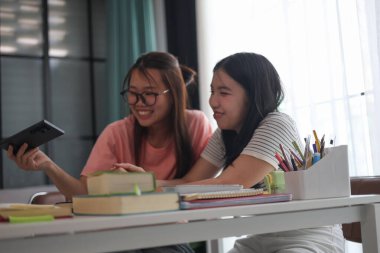 Evde ders çalışırken akıllı telefon kullanan iki kız öğrenci..