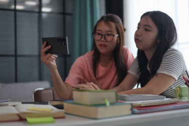 Evde ders çalışırken akıllı telefon kullanan iki kız öğrenci..