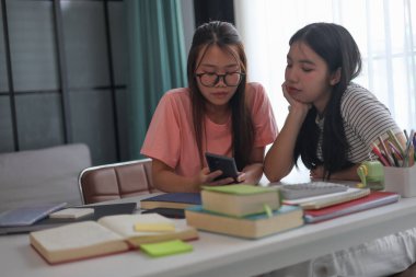 Evde ders çalışırken akıllı telefon kullanan iki kız öğrenci..