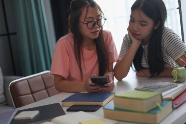 Evde ders çalışırken akıllı telefon kullanan iki kız öğrenci..