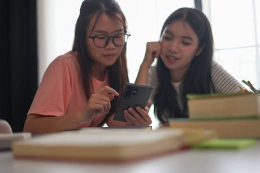 Evde ders çalışırken akıllı telefon kullanan iki kız öğrenci..