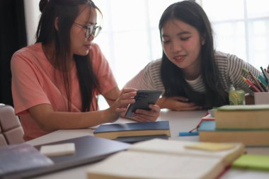 Evde ders çalışırken akıllı telefon kullanan iki kız öğrenci..