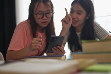 Evde ders çalışırken akıllı telefon kullanan iki kız öğrenci..