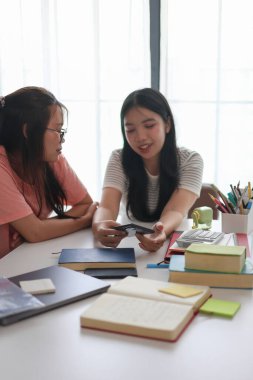 Evde ders çalışırken akıllı telefon kullanan iki kız öğrenci..
