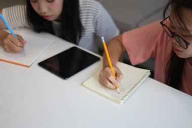 İki genç kız evde ders çalışırken not defterlerine yazıyorlar..