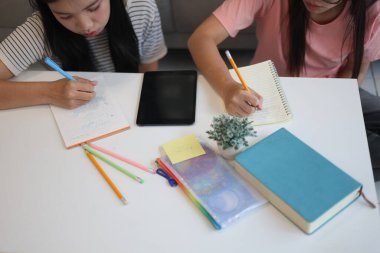 İki genç kız evde ders çalışırken not defterlerine yazıyorlar..