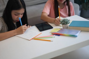 İki genç kız evde ders çalışırken not defterlerine yazıyorlar..