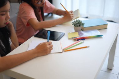 İki genç kız evde ders çalışırken not defterlerine yazıyorlar..