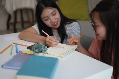 İki genç kız evde ders çalışırken not defterlerine yazıyorlar..