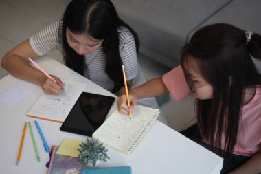 İki genç kız evde ders çalışırken not defterlerine yazıyorlar..