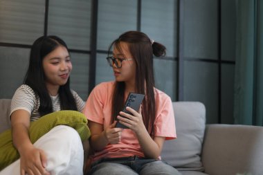 İki Asyalı genç kız arkadaş telefon ekranı paylaşımına bakıyorlar..