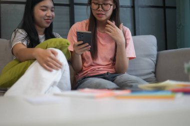 İki Asyalı genç kız arkadaş telefon ekranı paylaşımına bakıyorlar..