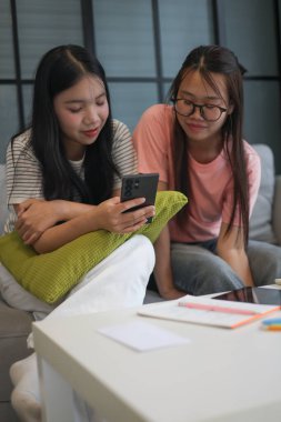 İki Asyalı genç kız arkadaş telefon ekranı paylaşımına bakıyorlar..