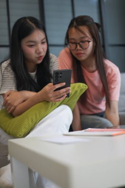 İki Asyalı genç kız arkadaş telefon ekranı paylaşımına bakıyorlar..