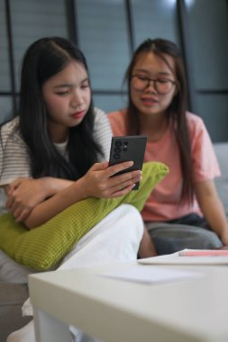 İki Asyalı genç kız arkadaş telefon ekranı paylaşımına bakıyorlar..