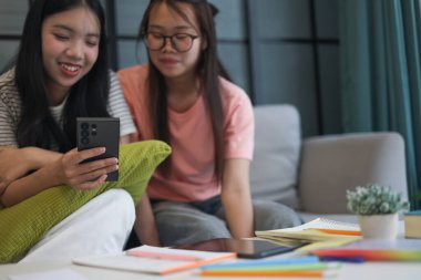 İki Asyalı genç kız arkadaş telefon ekranı paylaşımına bakıyorlar..