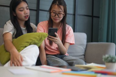 İki Asyalı genç kız arkadaş telefon ekranı paylaşımına bakıyorlar..