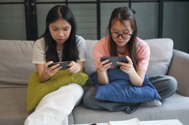 İki Asyalı kız arkadaş telefonda oyun oynuyorlar.