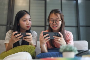 İki Asyalı kız arkadaş telefonda oyun oynuyorlar.
