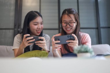 İki Asyalı kız arkadaş telefonda oyun oynuyorlar.