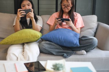 İki Asyalı kız arkadaş telefonda oyun oynuyorlar.