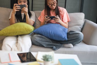 İki Asyalı kız arkadaş telefonda oyun oynuyorlar.