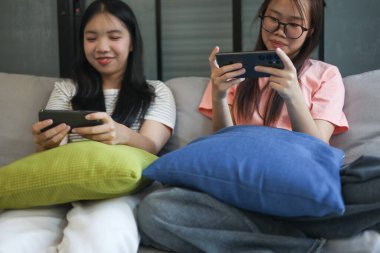 İki Asyalı kız arkadaş telefonda oyun oynuyorlar.