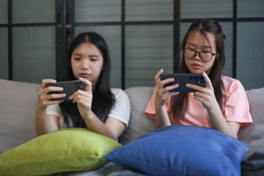 İki Asyalı kız arkadaş telefonda oyun oynuyorlar.