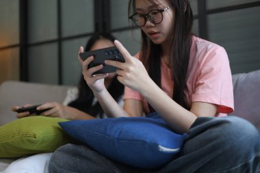 İki Asyalı kız arkadaş telefonda oyun oynuyorlar.