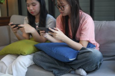 İki Asyalı kız arkadaş telefonda oyun oynuyorlar.