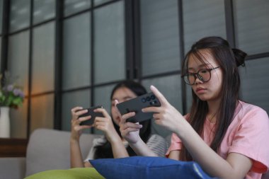 İki Asyalı kız arkadaş telefonda oyun oynuyorlar.