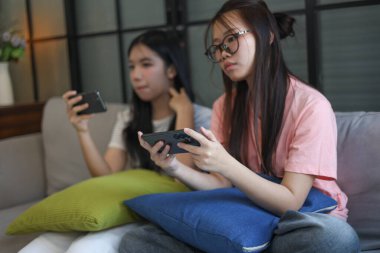 İki Asyalı kız arkadaş telefonda oyun oynuyorlar.