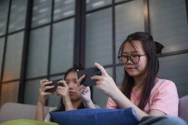 İki Asyalı kız arkadaş telefonda oyun oynuyorlar.