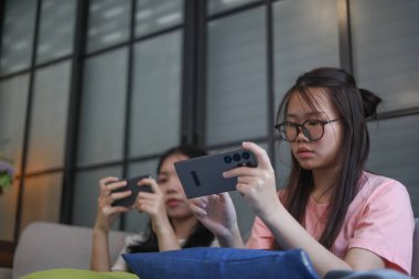 İki Asyalı kız arkadaş telefonda oyun oynuyorlar.