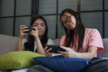 İki Asyalı kız arkadaş telefonda oyun oynuyorlar.