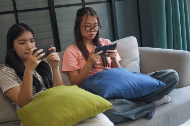 İki Asyalı kız arkadaş telefonda oyun oynuyorlar.