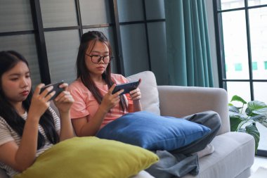 İki Asyalı kız arkadaş telefonda oyun oynuyorlar.