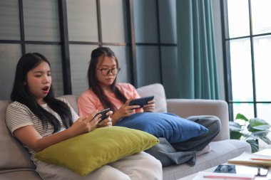 İki Asyalı kız arkadaş telefonda oyun oynuyorlar.