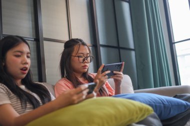 İki Asyalı kız arkadaş telefonda oyun oynuyorlar.