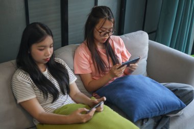 İki Asyalı kız arkadaş telefonda oyun oynuyorlar.