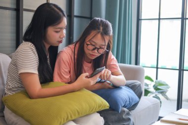 İki Asyalı genç kız arkadaş telefon ekranı paylaşımına bakıyorlar..