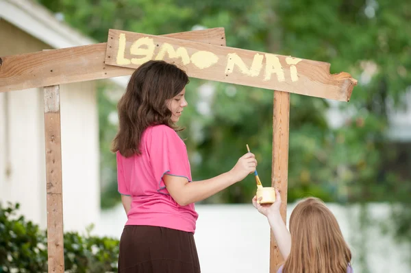 Two young girls painting a lemonade stand Stock Photo