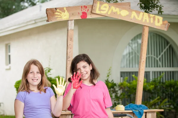 Two young girls painting a lemonade stand sign — 图库照片