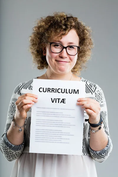 Krullend vrouw toont haar CV op een grijze achtergrond — Stockfoto