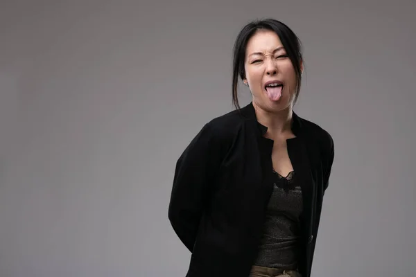 ソーシー失礼なアジア人女性アウト彼女の舌として彼女を見ますザカメラ上の灰色のスタジオの背景とともにCopyspace — ストック写真