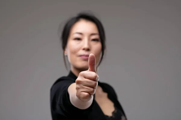 一个成功的有动力的女人 在一个灰色的工作室背景上 带着一个安静而快乐的微笑做着一个大拇指的手势和一个有版权的工作室背景 — 图库照片