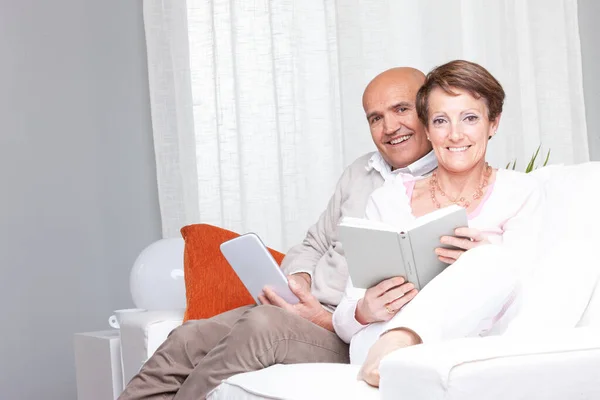 Married Couple Relaxing Home Sofa Reading Tablet Book Looking Camera — Stockfoto