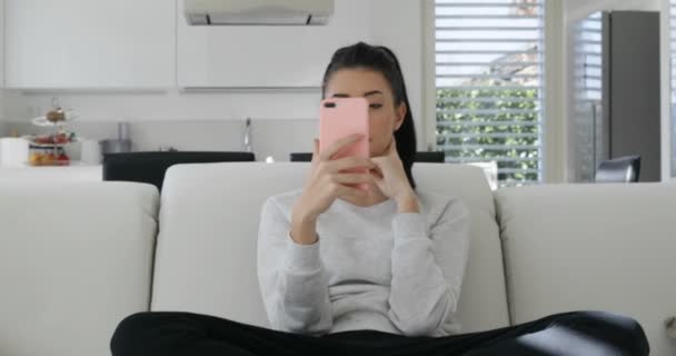 Mladá žena s růžovým telefonem na pohovce mluví — Stock video