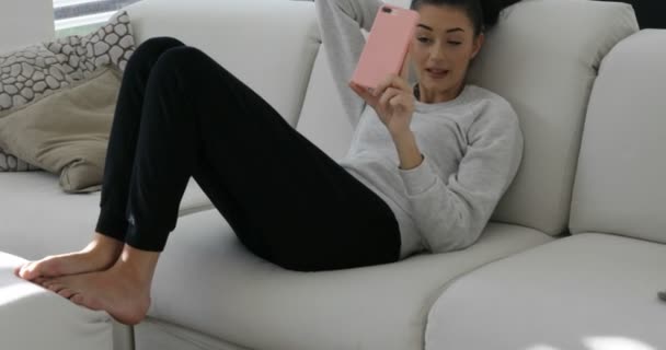 Mladá žena s růžovým telefonem na pohovce mluví — Stock video